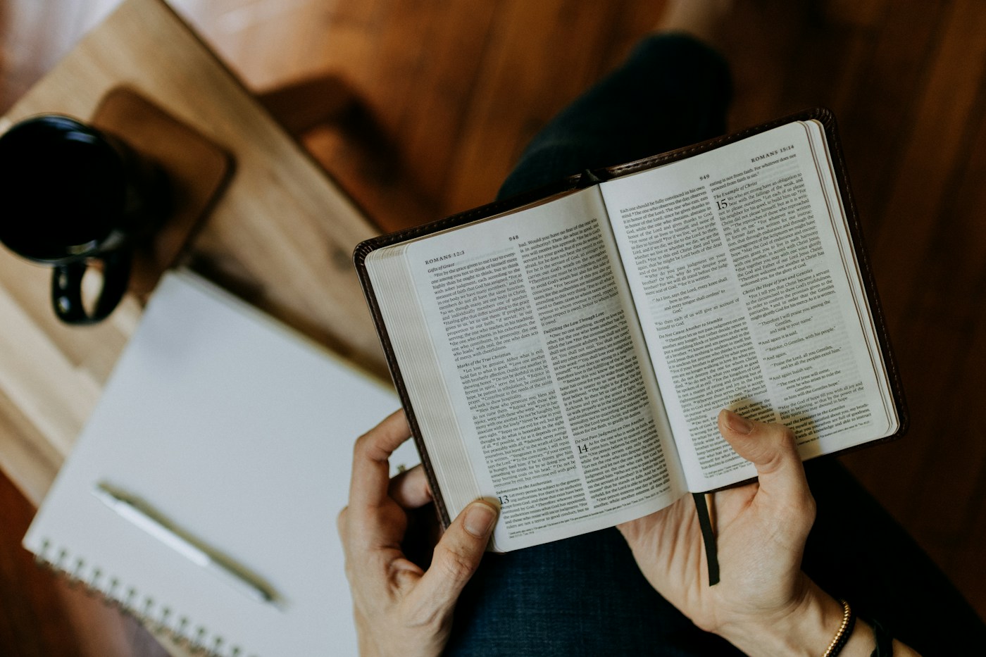 A reader studying an open Bible beside a notebook
